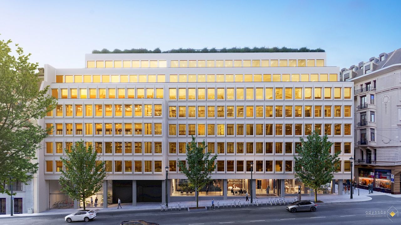 A modern office building with a bright, illuminated façade, surrounded by trees and urban street activity.